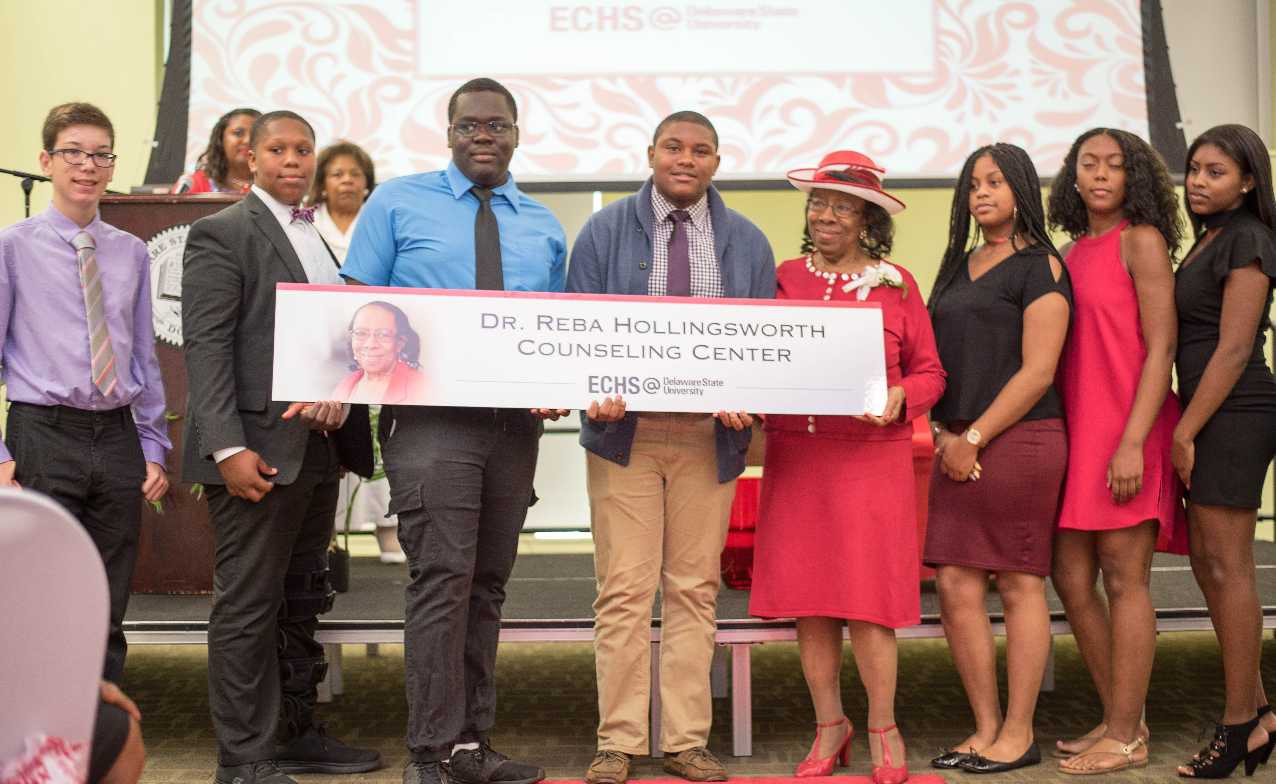 Dr. Reba Hollingsworth (in the red hat on the right side of the sign) is joined by students of the DSU Early College High School, as its counseling center is named after her.