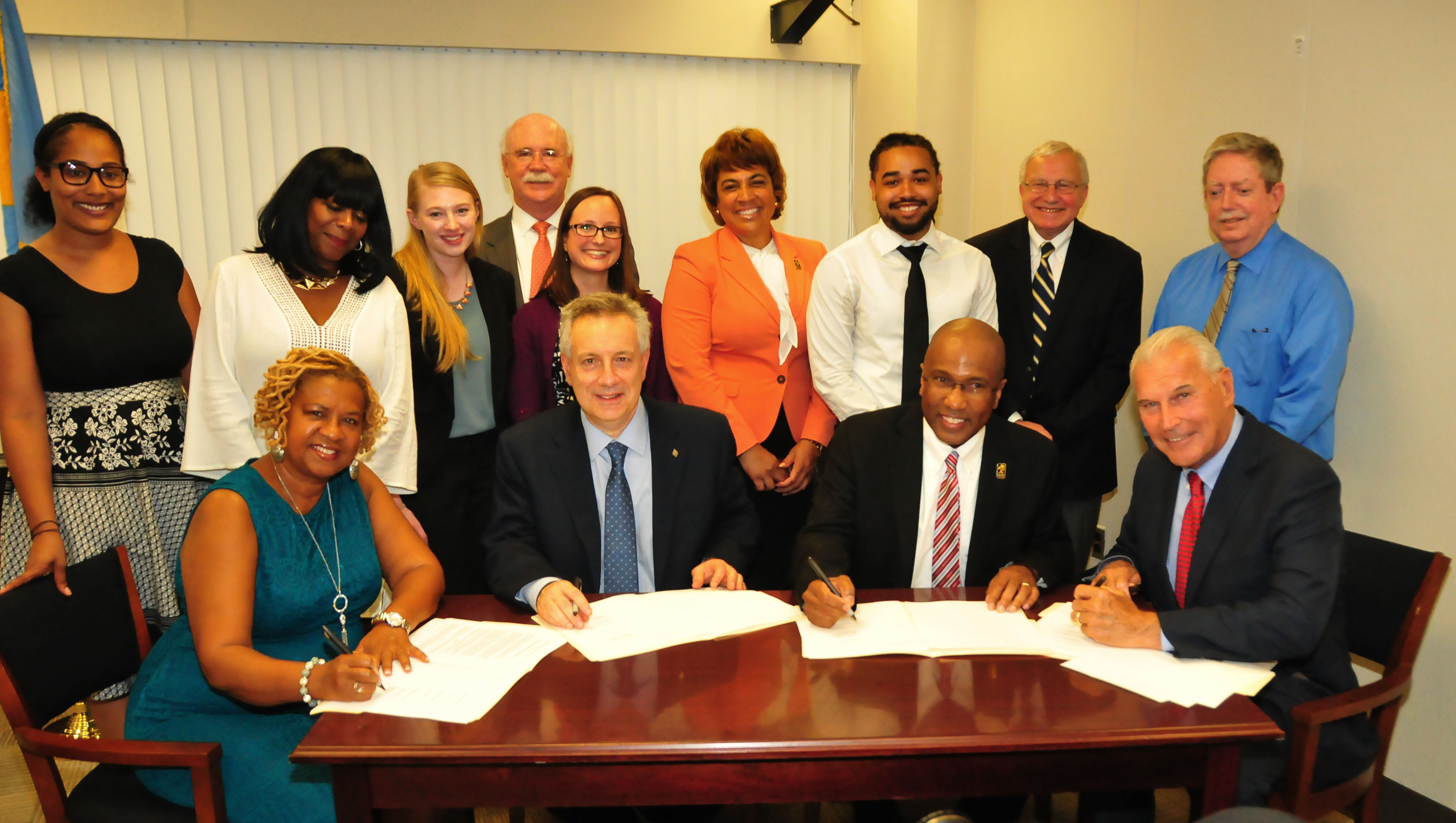(Seated l-r) Wilmington Council President Hanifa Shabazz, UD President Dennis Assanis, DSU President Harry L. Williams and Wilmington Mayor Mike Purzycki prepare to sign a cooperation and assistance agreement that will benefit the city, its residents and businesses. Representatives of UD, DSU and the city stand behind the signees.
